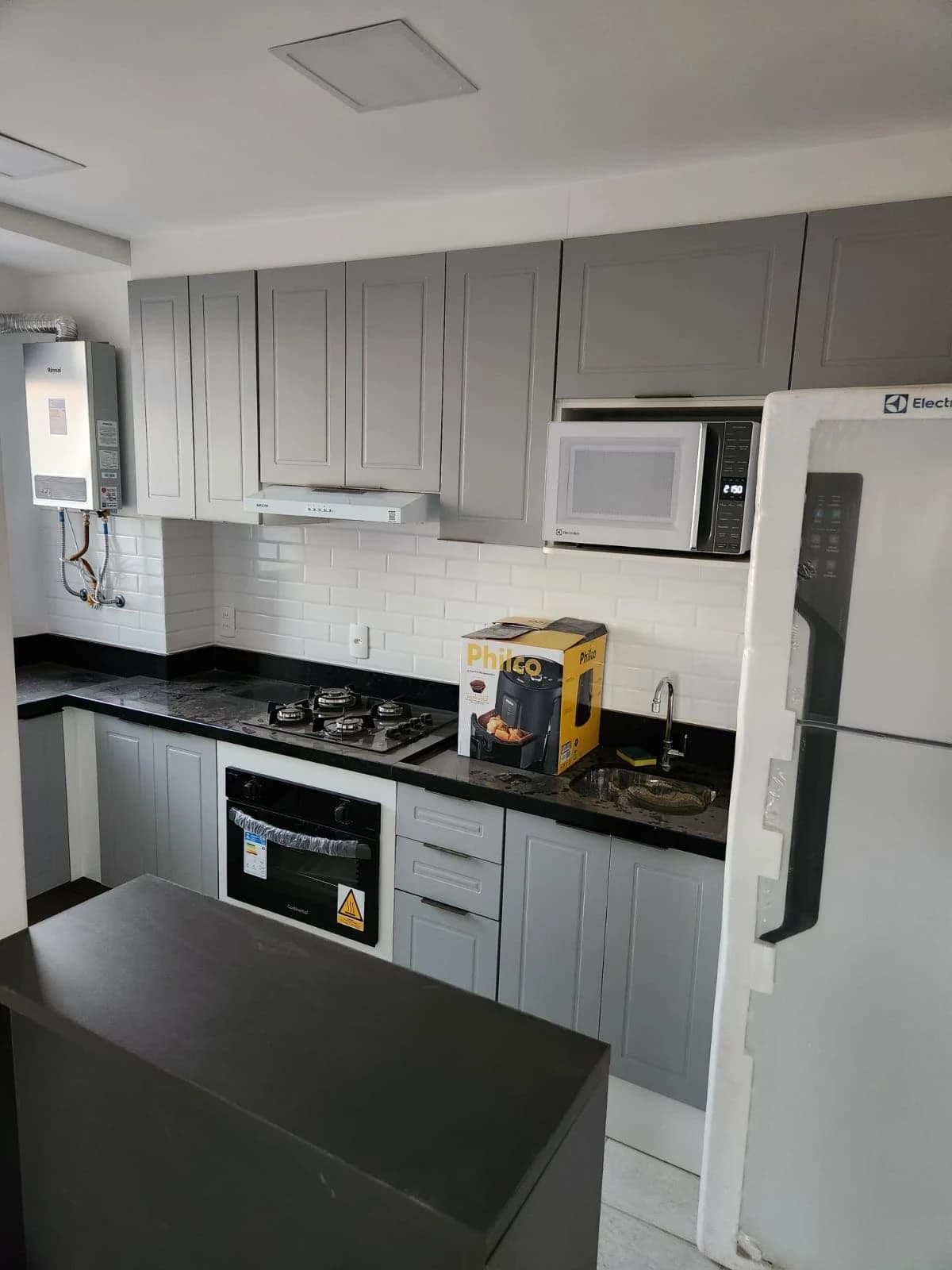 Cozinha Moderna em Tons Neutros: Ambiente contemporâneo com armários cinzas e bancada em granito preto. Destaque para a iluminação embutida e azulejos brancos, proporcionando funcionalidade e elegância.